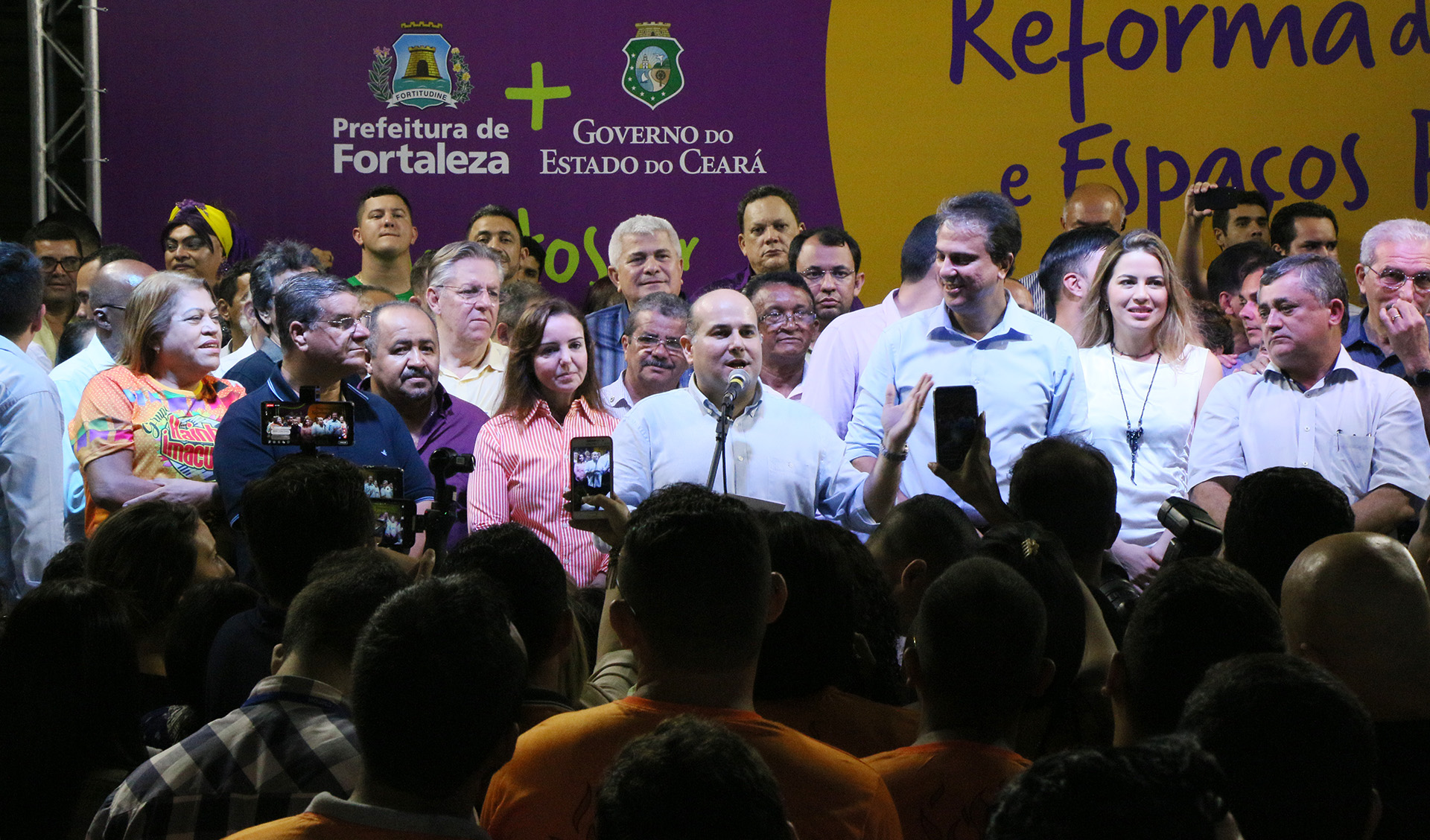 prefeito roberto cláudio fala ao microfone em um palco com dezenas de pessoas